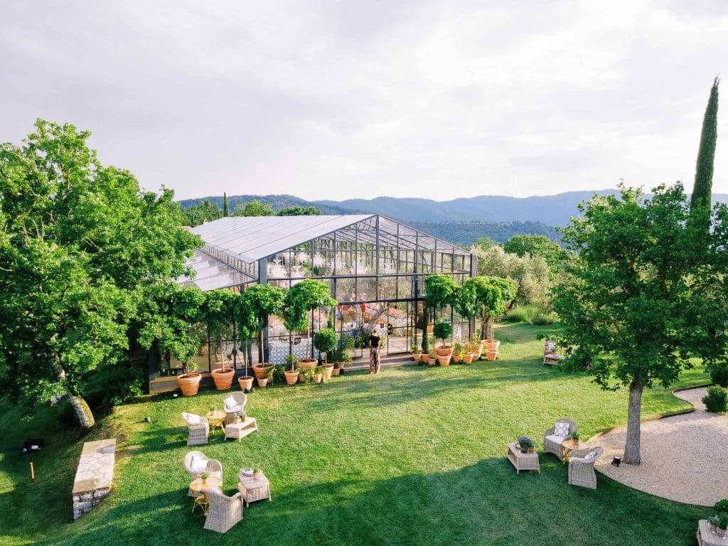 a greenhouse tent overlooks the mountains in Umbria, Italy. Potted trees flank the outer entrance, and cocktail seating is scattered on the lawn around the property. 